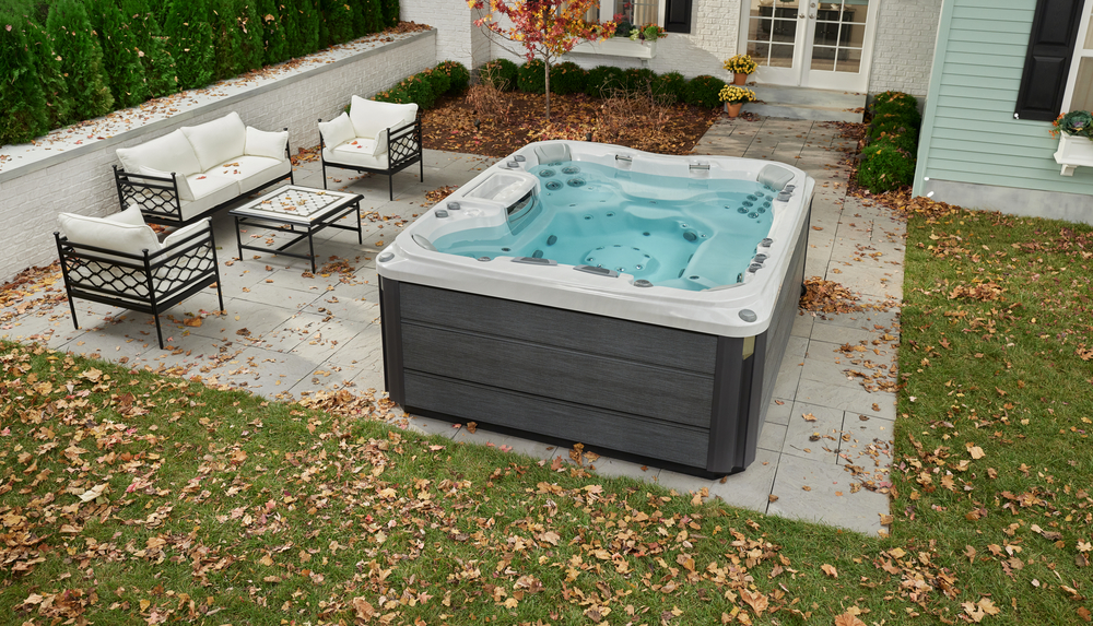 A hot tub in a backyard with a lounge chair and a fire pit