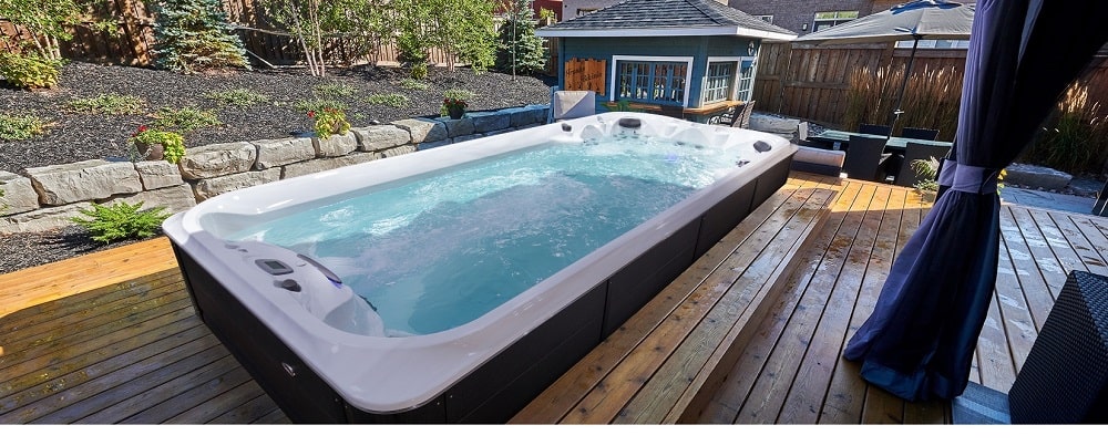 A backyard swimming spa with a wooden deck|taking swim spa in winter|woman is enjoying hydrotherapy session in swim spa