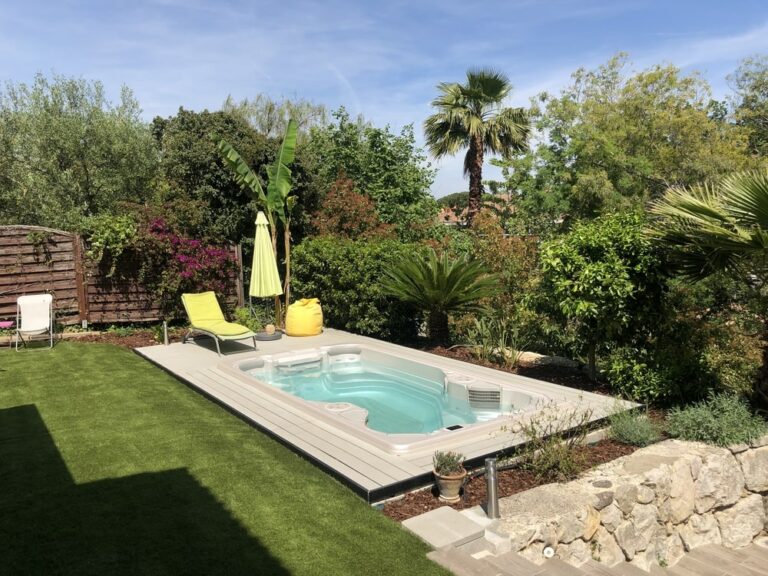 A backyard with a swim spa and a yellow umbrella||father is playing with kids in swim spa|A hot tub in a backyard with a pergola and blue lounge chairs