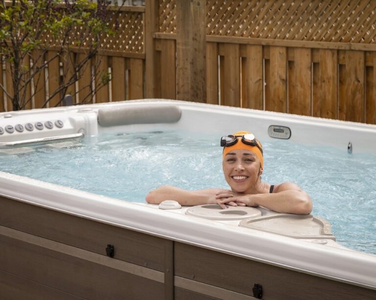 Person relaxing in an outdoor swim spa with swim cap and goggles|father is teaching his daughter how to swim in swimming spa|person swimming in a hydropool swim spa